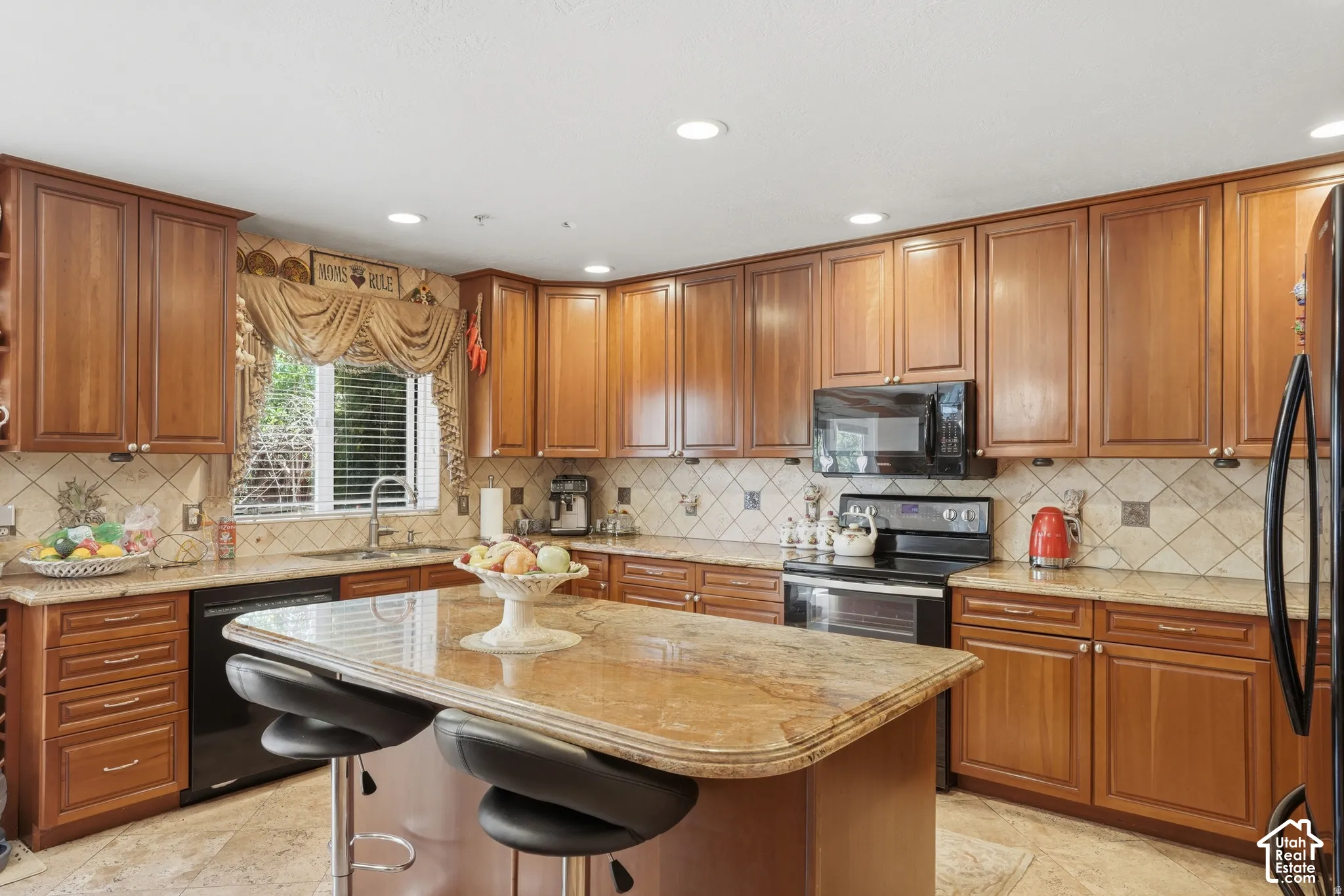 Kitchen featuring wood cabinetry, a center island with countertop seating, stainless steel sink, black appliances, and recessed lighting