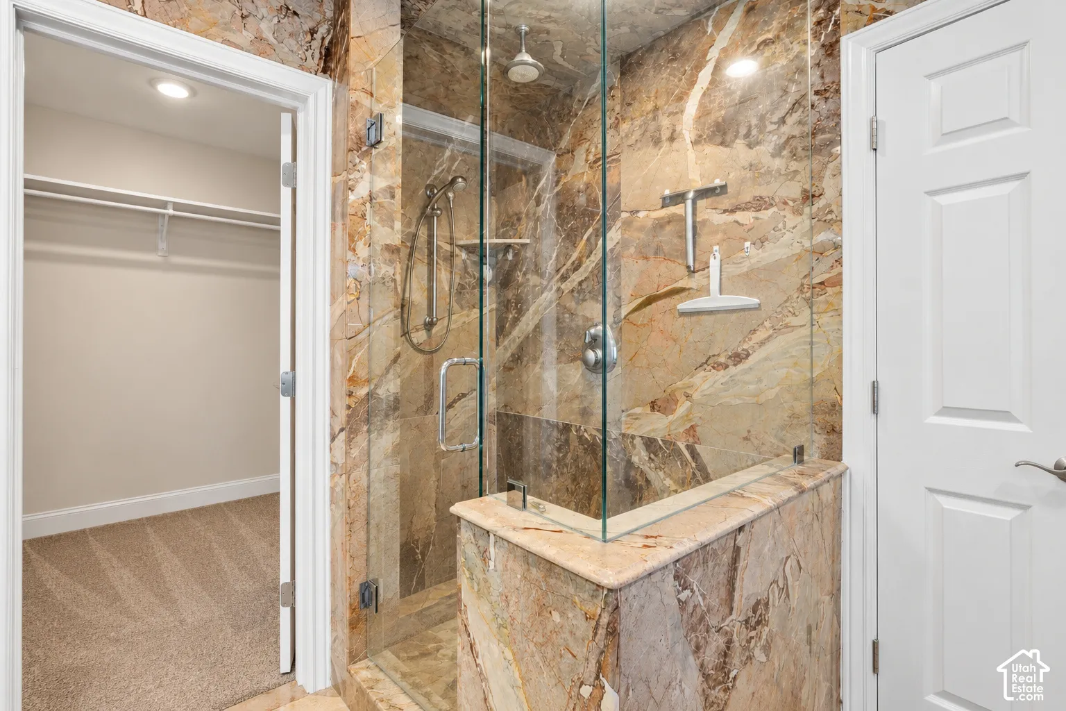 Glass-enclosed shower with a rainfall showerhead, handheld sprayer, and stone-finish tile surround