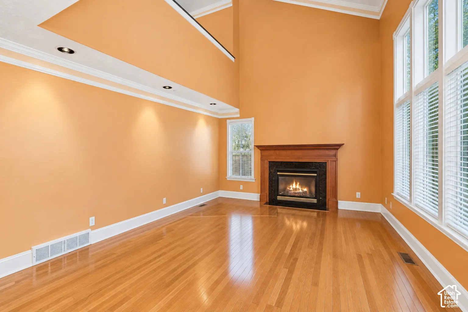 Hardwood flooring, fireplace with a wood mantle and dark stone surround, tall windows, crown molding, and recessed lighting