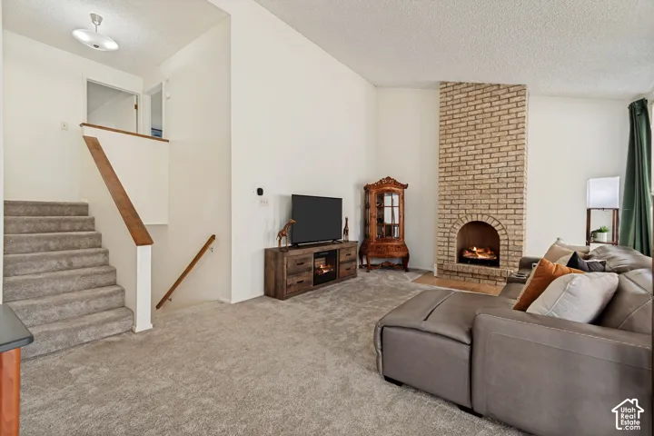 Living area featuring a brick-clad fireplace with an arched firebox, vaulted ceiling, and plush gray carpeting
