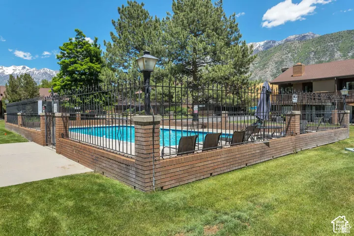Community pool with a black wrought iron fence and brick base, bordered by a concrete walkway and manicured lawn