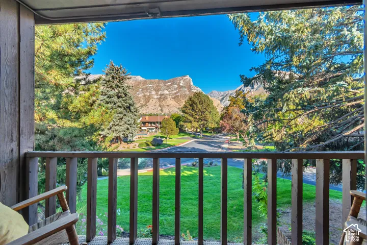 Balcony with wood railing, natural wood-finish siding, mountain backdrop, and mature trees