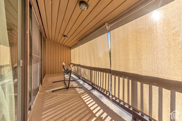 Covered balcony featuring wood-paneled walls and ceiling, privacy shades, and integrated lighting fixtures