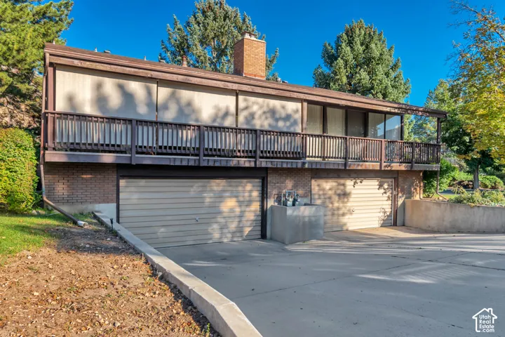 Brick and siding exterior featuring a full-width balcony with wood railing, floor-to-ceiling windows, and two garage doors