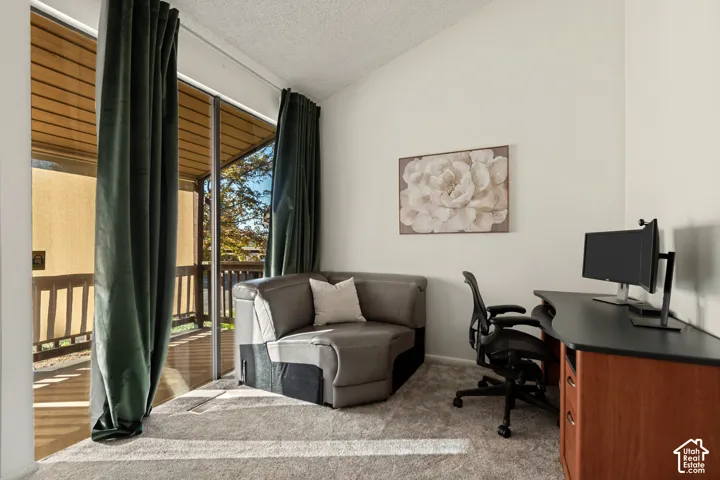 Sliding glass door, vaulted ceiling, and neutral carpet flooring