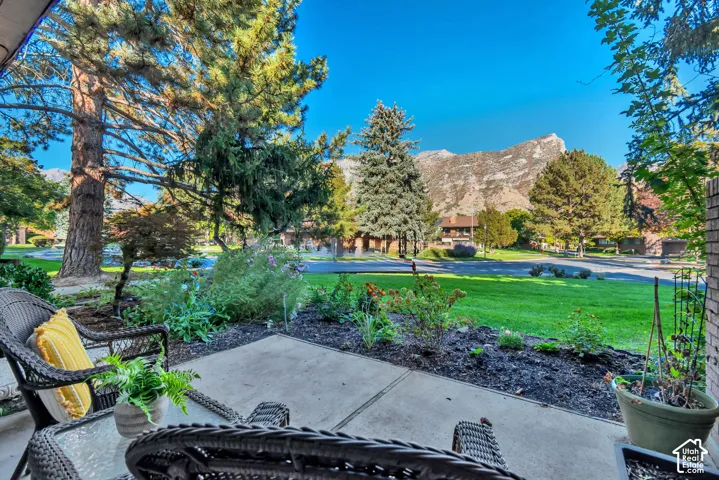 Paved patio with established landscaping, mature trees, manicured lawn, and mountain backdrop