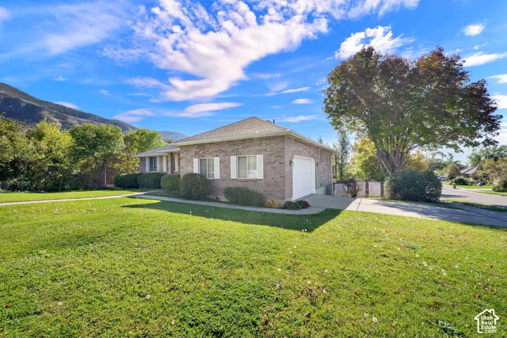 Brick exterior residence featuring a hipped roof, attached garage, concrete driveway, and established landscaping