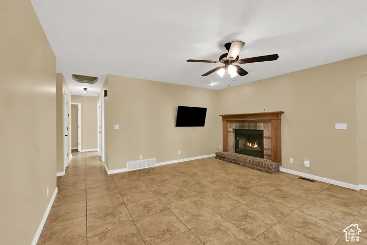 Living area featuring tile flooring, a brick fireplace with a wood mantel, and a ceiling fan