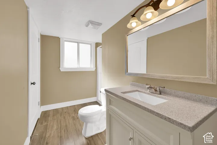 Bathroom featuring a wood-finish floor, white vanity cabinet with an integrated sink, speckled solid-surface countertop, and a multi-bulb vanity light fixture