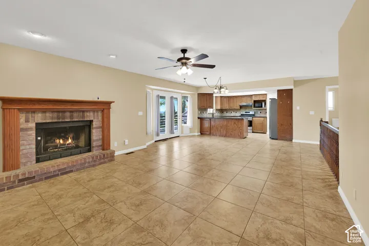 Open-concept interior featuring large-format tile flooring, a masonry fireplace with a wood mantel, glass-paneled double doors, wood cabinetry, and a ceiling fan