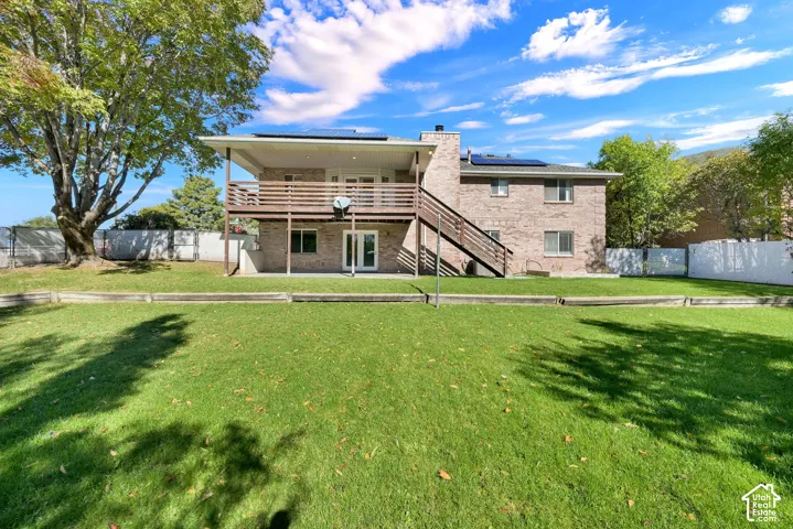 Multi-level brick exterior featuring a raised wood deck with an attached staircase, exterior solar panels, and a fenced backyard with mature trees