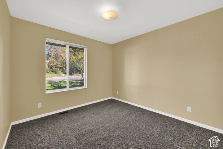 Neutral-toned walls, carpeted flooring, large window with exterior greenery, and a central flush-mount light fixture