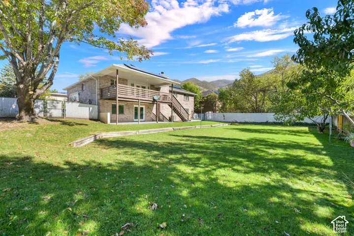 Expansive backyard featuring a tiered lawn, wood-railing deck, exterior staircase, and brick masonry siding, set against a mountain backdrop