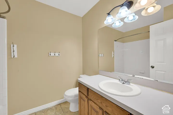 Bathroom featuring a single-sink vanity with a solid-surface countertop, full-width wall mirror, multi-bulb overhead lighting, and tile flooring