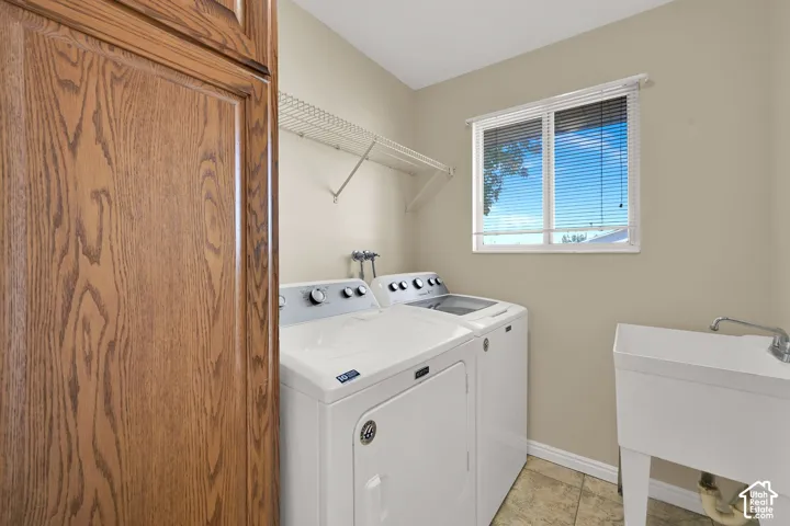 Laundry room featuring wood-finish cabinetry, a white utility sink, metal wire shelving, and tile flooring