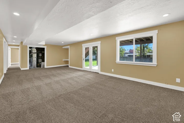 Open-concept room featuring wall-to-wall carpeting, recessed ceiling lighting, a large window with thick trim, and glass-paned doors leading to exterior grounds