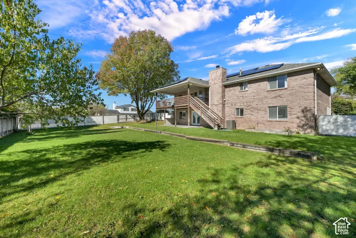 Spacious backyard with a manicured lawn, masonry exterior, elevated wood deck with stairs, exterior brick chimney, and rooftop solar panels