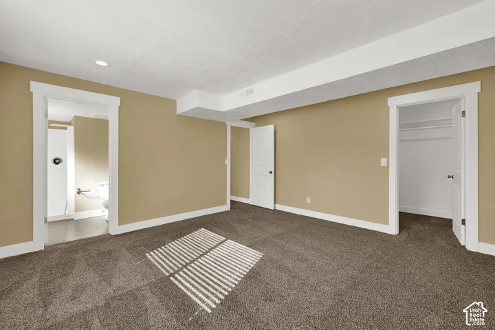 Neutral-toned room featuring wall-to-wall carpeting, white interior trim, recessed lighting, and access to a full bathroom and walk-in closet