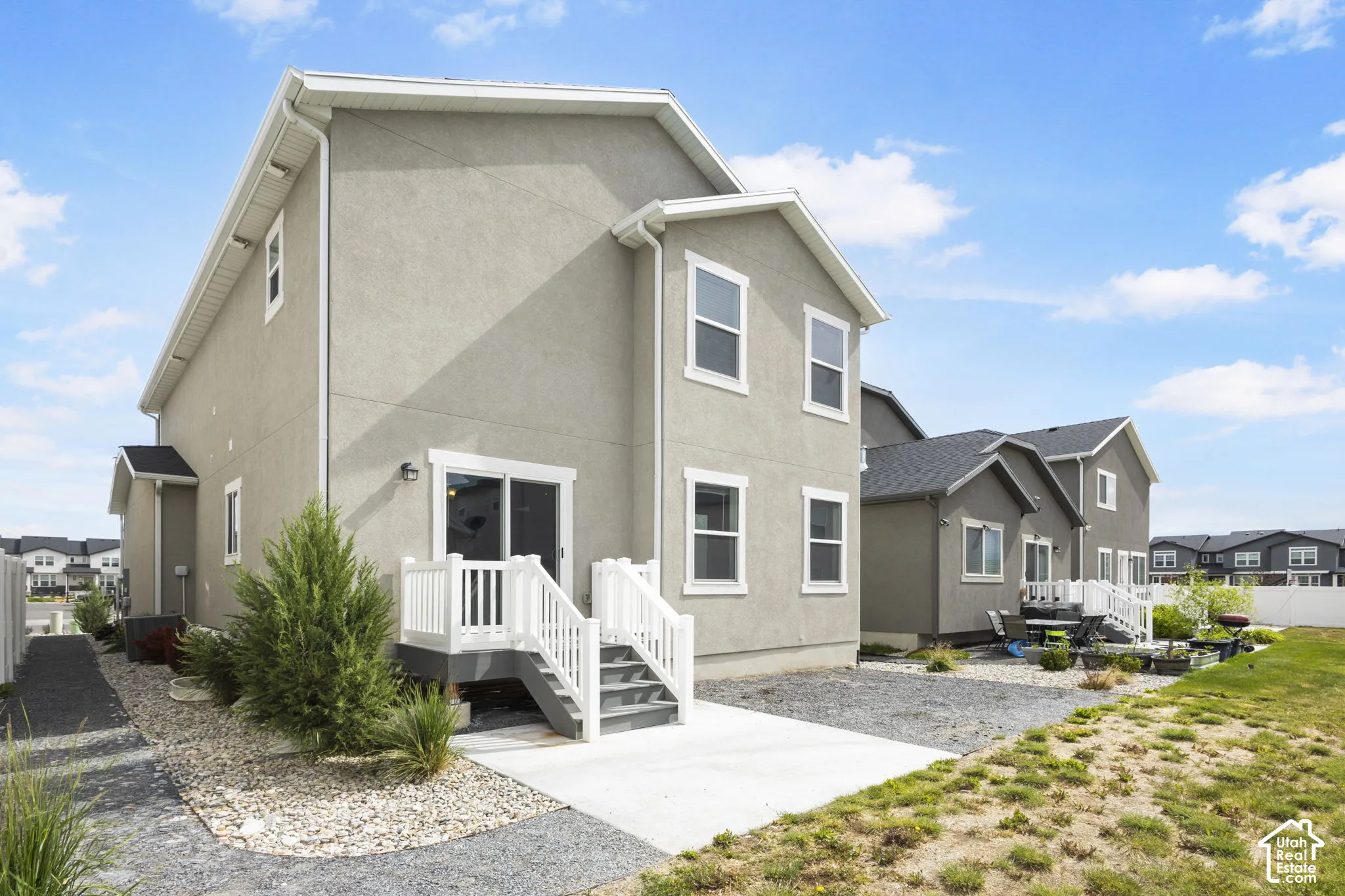 Stucco exterior with white trim, a rear concrete patio, white deck with steps, and a gravel-lined pathway