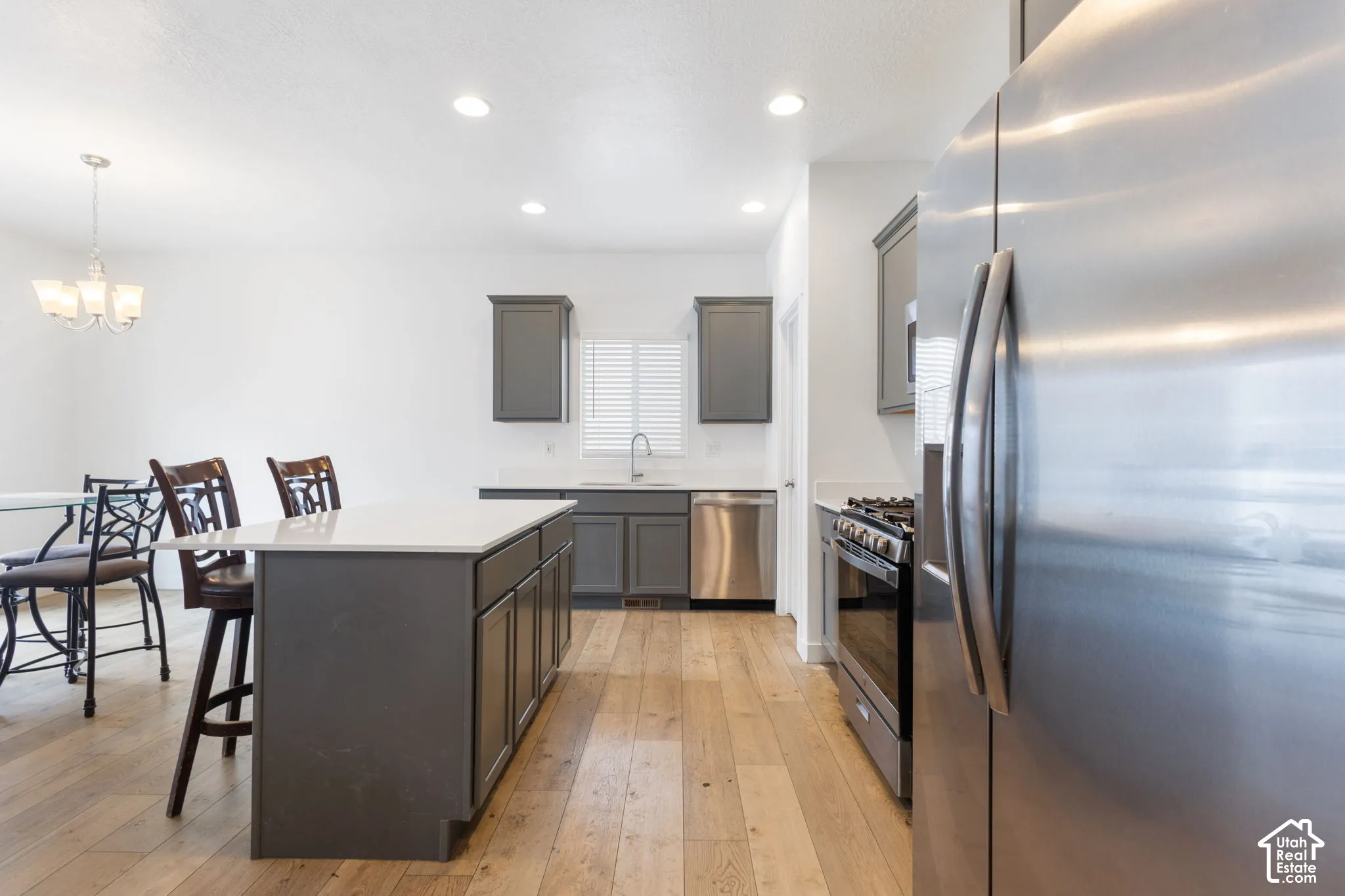 Open-concept kitchen featuring wood-finish flooring, dark grey cabinetry, white countertops, and stainless steel appliances