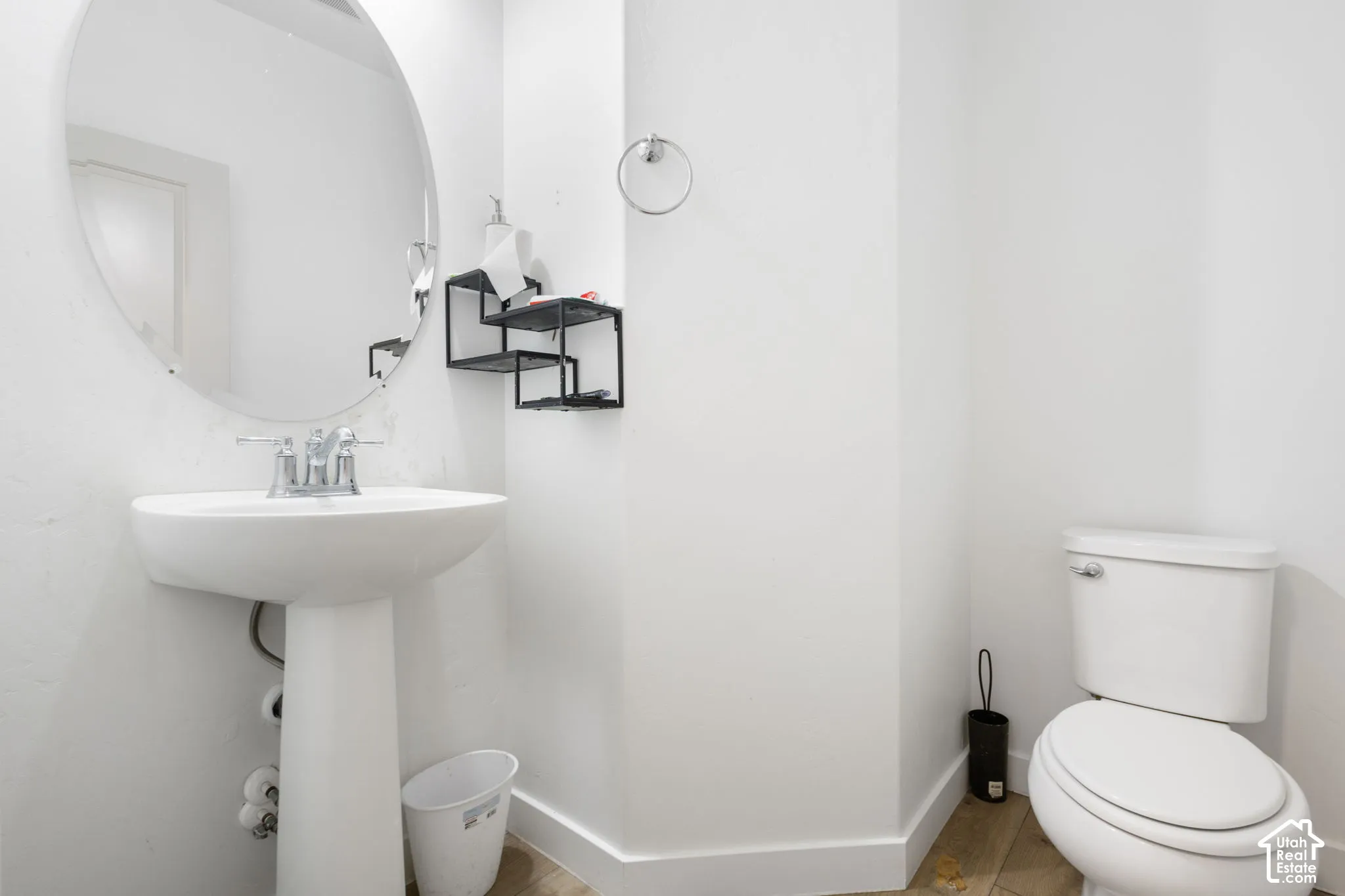 White pedestal sink with chrome faucet, circular mirror, and wood-finish flooring