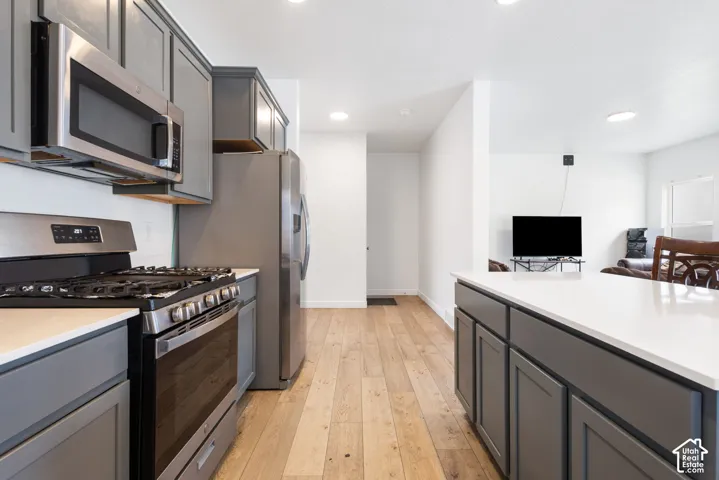 Kitchen featuring stainless steel appliances, grey cabinetry, white countertops, and wood-finish flooring