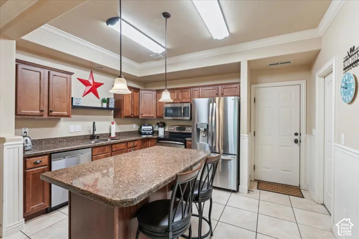 Kitchen featuring wood-finish cabinetry, granite countertops, tile flooring, stainless steel appliances, and a central island with pendant lighting