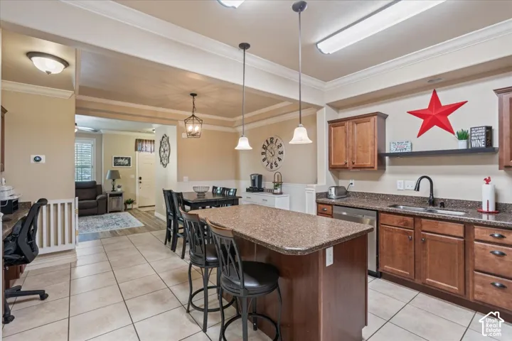 Kitchen featuring an island with seating, a stainless steel dishwasher, a black gooseneck faucet, light brown cabinetry, and tiled flooring
