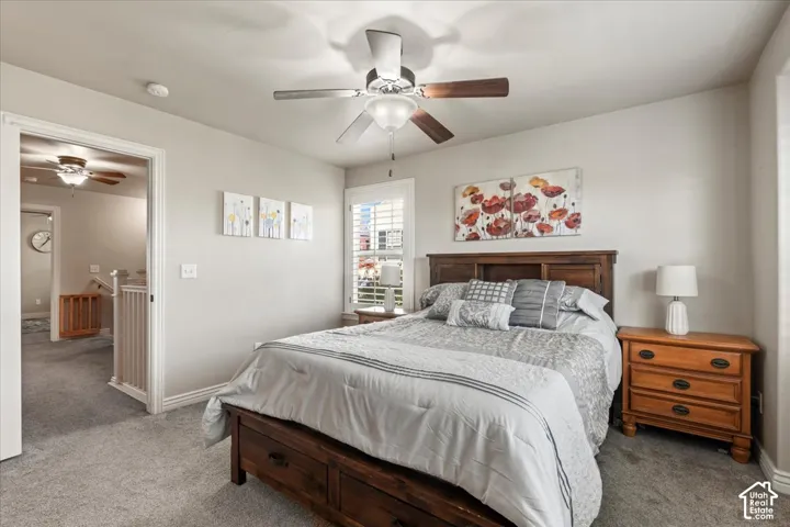 Ceiling fan with light fixture, carpeted flooring, window with white plantation shutters, built-in wooden headboard, and solid core door