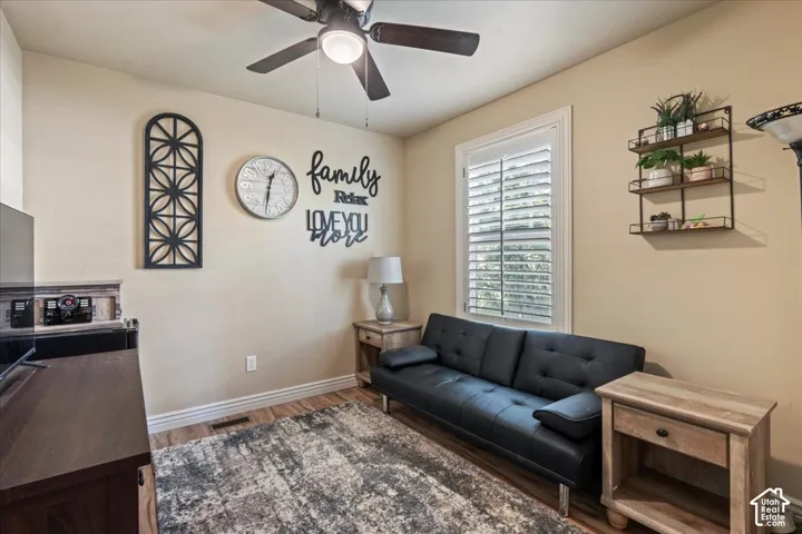 Wood-finish flooring, ceiling fan with integrated lighting, window with plantation shutters, and a wall-mounted shelving unit