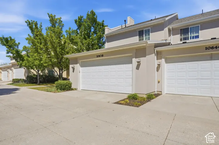 Stucco exterior featuring dual panel garage doors, concrete driveways, and mature landscaping