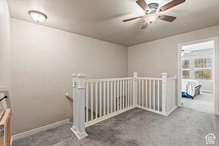 Carpeted landing with white balusters, a ceiling fan with integrated lighting, and a flush-mount light fixture