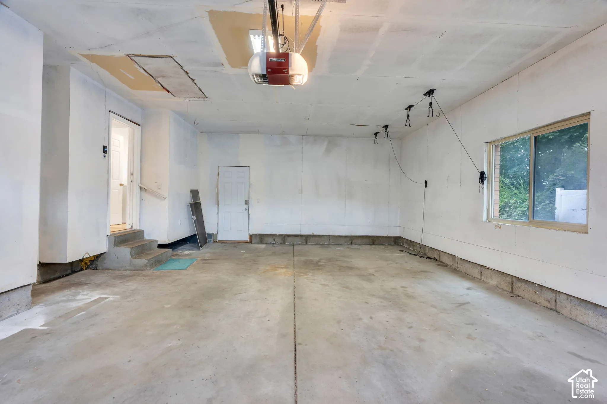 Concrete flooring with a white paneled ceiling, featuring a garage door opener system, multiple wall-mounted hooks, and a window