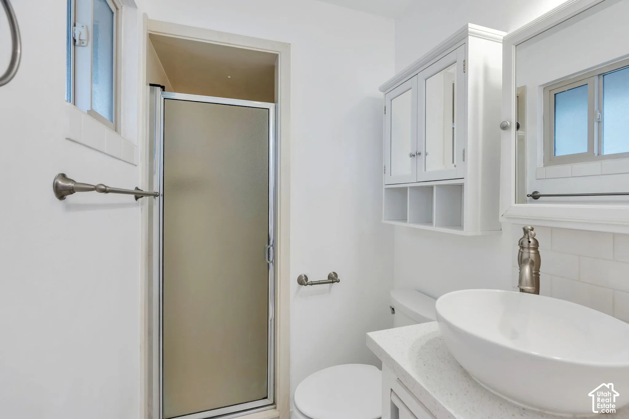Frosted glass shower enclosure, a vessel sink, white subway tile backsplash, and a wall-mounted medicine cabinet with open shelving