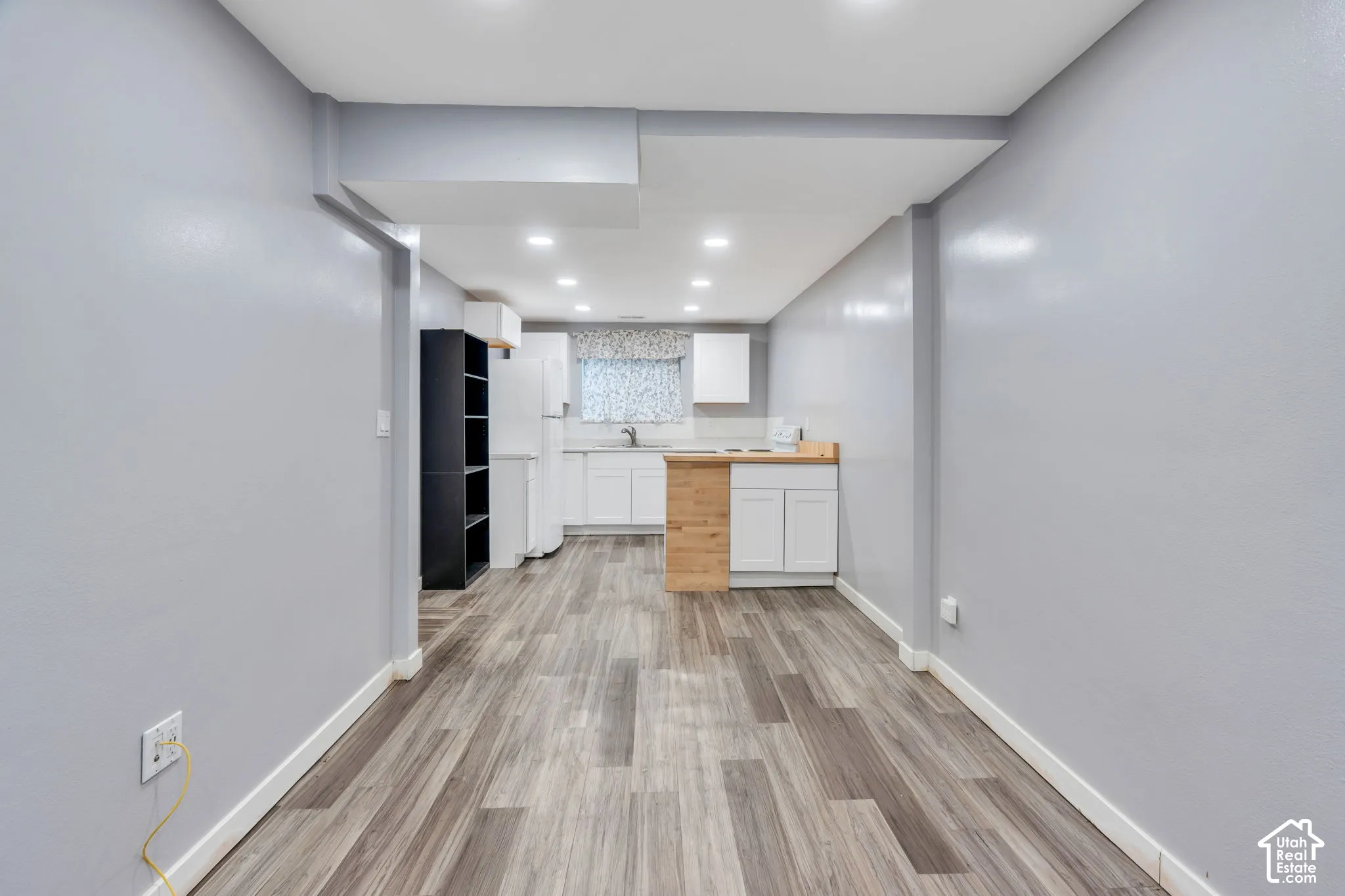 Wood-finish flooring throughout, recessed lighting, and a kitchen area featuring white cabinetry and light-toned countertops