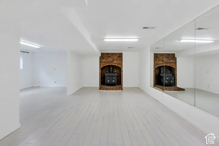 Spacious room featuring light wood-finish flooring, a brick-surround fireplace with a hearth, full-height wall mirrors, and recessed lighting
