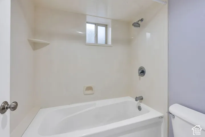 White bathtub with integrated shower, chrome fixtures, and a corner shelf