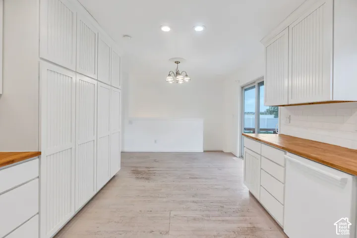 White cabinetry, wood-finish countertops, subway tile backsplash, recessed lighting, and a sliding glass door