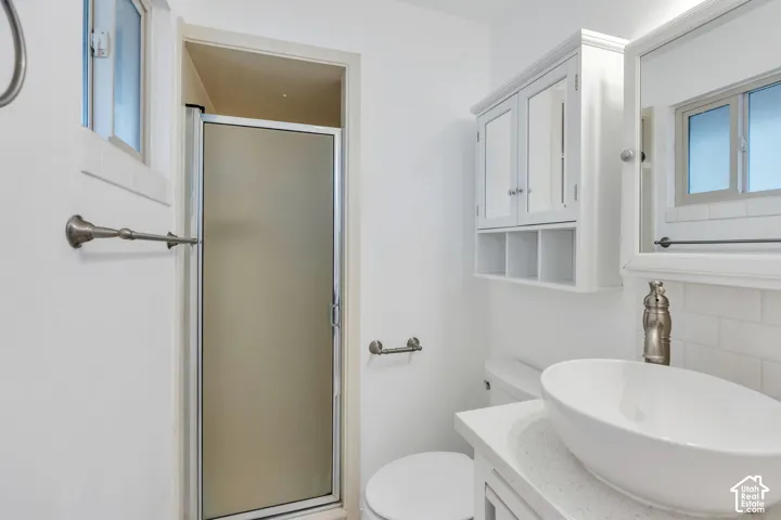 Frosted glass shower enclosure, a vessel sink, white subway tile backsplash, and a wall-mounted medicine cabinet with open shelving