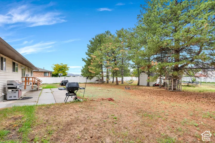 Spacious backyard with mature shade trees and level grounds, featuring a gas grill and outdoor entertaining space