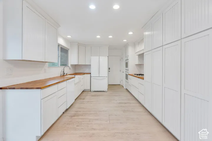 White cabinetry with beadboard paneling, wood-finish countertops, light wood-finish flooring, recessed lighting, and white subway tile backsplash