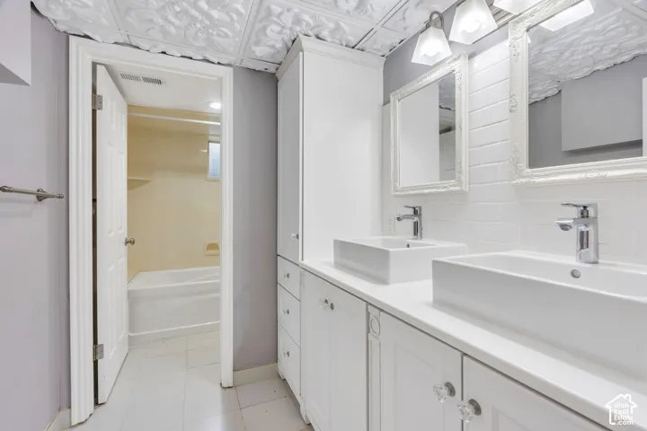 Double vanity with vessel sinks and chrome faucets, white cabinetry with clear hardware, white subway tile backsplash, and a white embossed ceiling