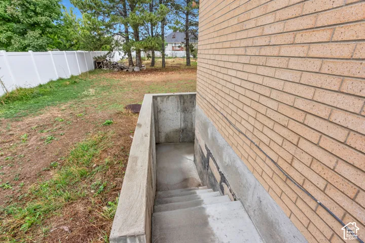 Brick exterior with a concrete foundation, concrete basement access, and a white privacy fence