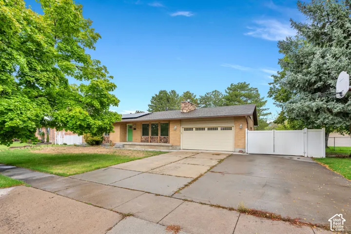 Brick exterior with a prominent chimney, attached garage with sectional door, paved driveway, and perimeter fencing