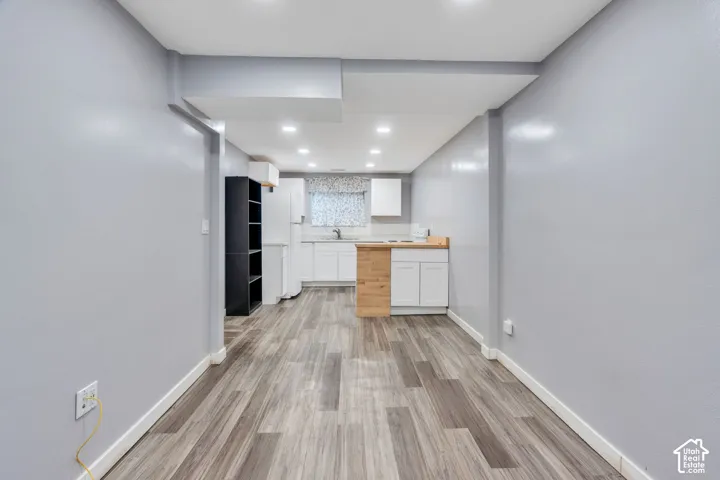 Wood-finish flooring throughout, recessed lighting, and a kitchen area featuring white cabinetry and light-toned countertops
