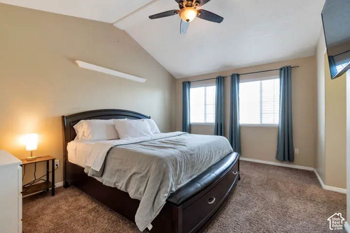 Vaulted ceiling with a ceiling fan, two windows, wall-mounted television, and carpeted flooring