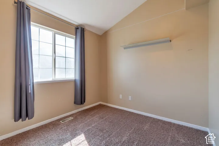 Vaulted ceiling, grid-pattern window, neutral-toned carpeting, light-toned wall paint, built-in lighting fixture