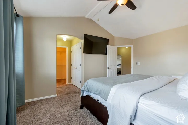 Vaulted ceiling with a ceiling fan, arched doorway, and carpet flooring