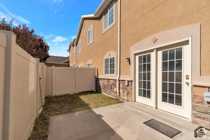 Stucco exterior with stone veneer accents, double French doors, concrete patio, and privacy fencing