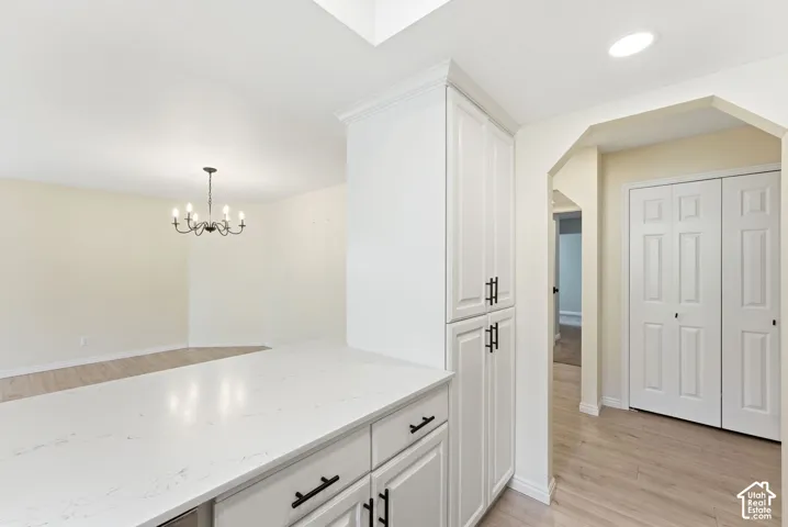 White shaker cabinetry with matte black hardware, light-toned wood-finish flooring, white countertop, recessed lighting, and a chandelier with a dark finish